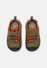 Grüne Wildlederschuhe mit orangefarbener Netzinnenauskleidung, elastischen Schnürsenkeln und schwarzen Gummisohlen. Mit einem Klettverschluss für einfaches An- und Ausziehen.