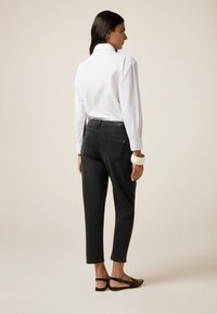 Camisa blanca de manga larga, jeans negros ajustados cortos, textura suave, bolsillos traseros, sandalias negras, fondo claro.