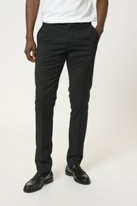 Pantalons noirs ajustés avec une coupe slim, présentant un devant plat, des passants de ceinture et des poches latérales, associés à des mocassins noirs brillants.