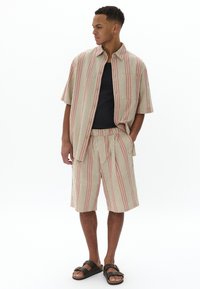 Camisa de manga corta a rayas en crema, rojo y verde con un bolsillo en el pecho, combinada con shorts a juego y sandalias negras. Ajuste casual y relajado.