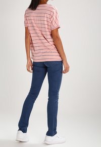 Růžové pruhované tričko s krátkým rukávem, spárované s tmavě modrými úzkými džíny a bílými teniskami, z pohledu zezadu.