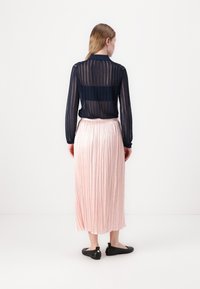 Marineblå, gjennomsiktig skjorte med lange ermer og vertikale striper, kombinert med et rosa, plissert maxiskjørt. Svarte leiligheter fullfører antrekket.