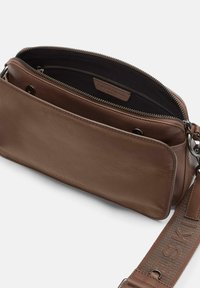 Brown leather crossbody bag with a zippered main compartment, fabric lining, and a textured strap featuring embossed letters.