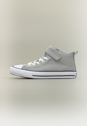 Zapatilla bota alta gris claro con suela de goma blanca, cordones blancos, una tira de velcro y ribete negro sobre un fondo neutro.