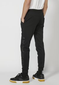 Sorte svedbukser med en tapered design, elastisk talje, sidelommer og et reflekterende print langs venstre ben.