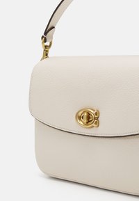 Borsa a tracolla in pelle crema con finitura testurizzata, hardware dorato e chiusura a soffietto arrotondata. Presenta una tracolla con dettagli marroni.