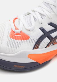 Witte sportieve schoen met een gestructureerde mesh bovenkant, oranje en marineblauwe accenten, en zichtbare logodetails op de middenzool met "FFBlast+" branding.