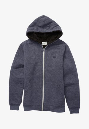 Granatowa bluza z zamkiem na całej długości, z kapturem wyłożonym sztucznym futrem, dwoma przednimi kieszeniami, ściągaczami na rękawach i małym logo Billabong na piersi. Miękka tkanina.