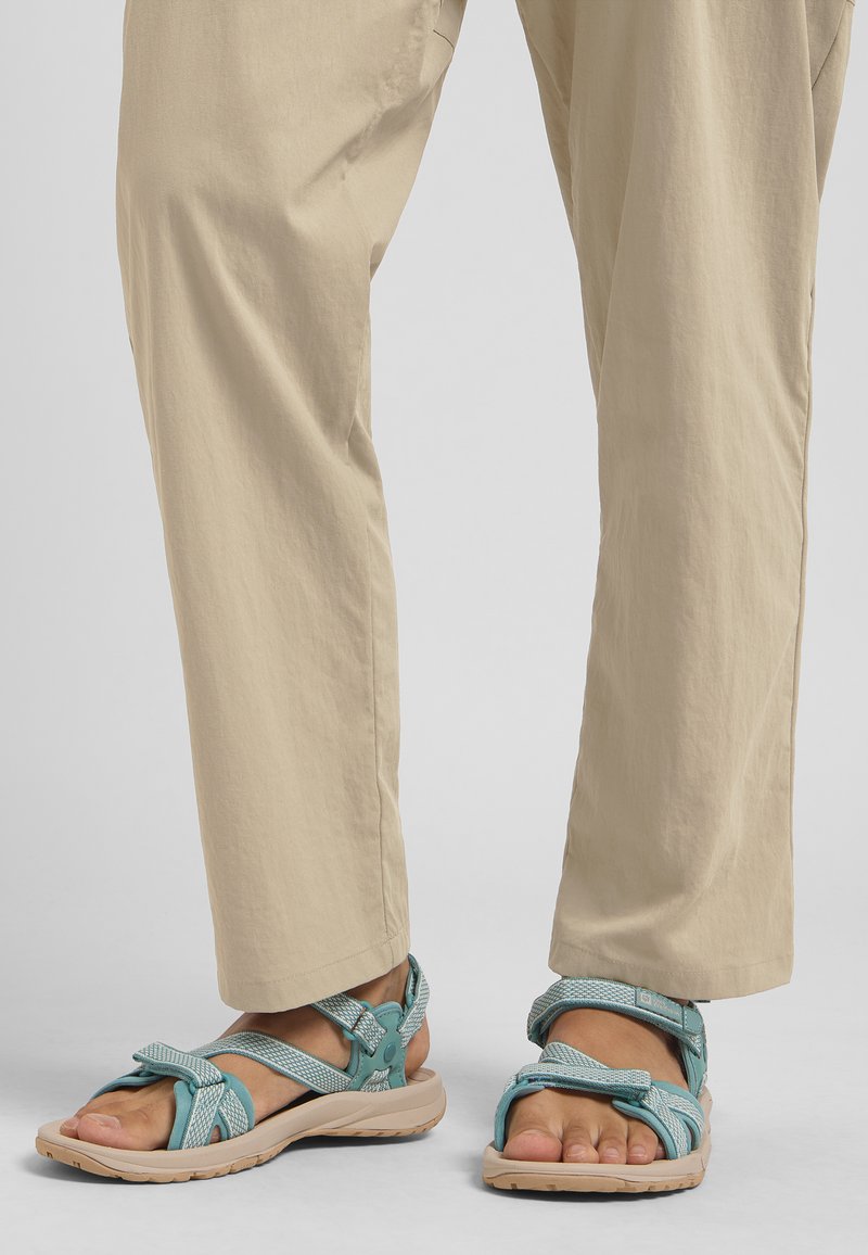Turquoise sandals with adjustable straps, textured fabric, and a cushioned sole. Worn with light beige, loose-fitting trousers.