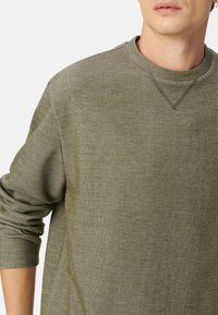 Grüner strukturierter Pullover mit Rundhalsausschnitt, gerippten Bündchen und seitlichen Nähten, der einen weichen Stoff und ein lässiges Design zeigt.