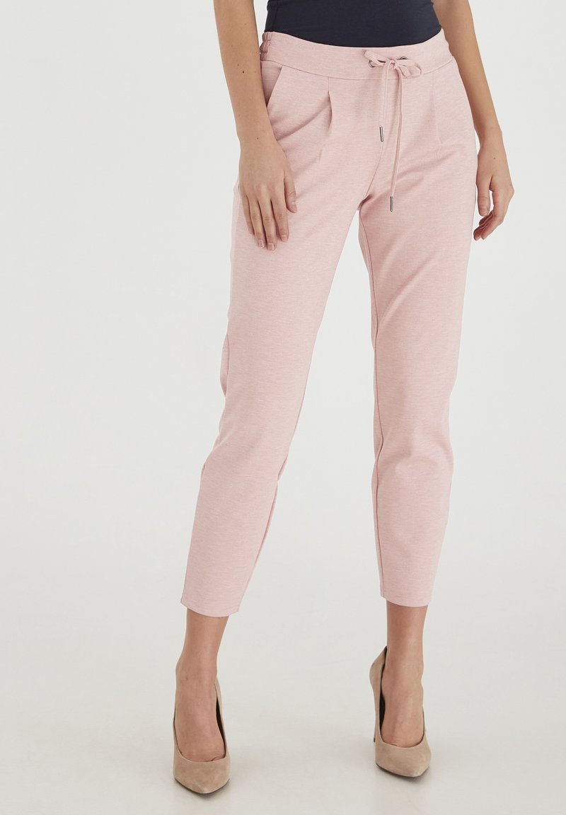 Jasnoróżowe spodnie dresowe wykonane z miękkiego materiału, z elastycznym pasem w talii i sznurkiem, oraz bocznymi kieszeniami. Dopasowana długość do kostek.
