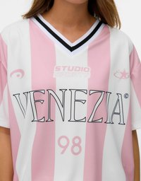 Kortærmet trøje i pink og hvid stribet med V-hals, som har "STUDIO SPORTS" og "VENEZIA" i fremtrædende sort skrift. Nummer 98 nedenfor.