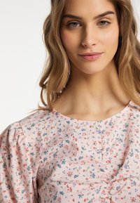 Bluse med blomstermønster i blødt pink stof, med rund halsudskæring og puffede ærmer. Materialet ser tekstureret ud med fine detaljer.