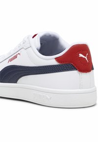 Białe trampki z granatowym paskiem i czerwonym akcentem na pięcie. Posiadają syntetyczną cholewkę, płaskie sznurówki oraz teksturowaną gumową podeszwę. Logo umieszczone z boku i na pięcie.