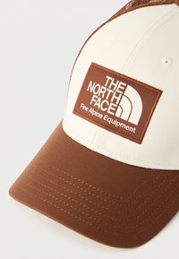 Καφέ και μπεζ δίχρωμο καπέλο μπέιζμπολ με ορθογώνιο λάστιχο που φέρει το λογότυπο "THE NORTH FACE Fine Alpine Equipment" στην εμπρόσθια πλευρά.