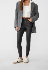 Šedý kostkovaný blejzr přes bílý žebrovaný crop top, v kombinaci s černými skinny kalhotami a béžovými teniskami s černými akcenty. Hladké textury.