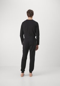 Black, long-sleeve pajama set with a relaxed fit and elastic waistband. Features smooth texture and tapered cuffs at ankles.