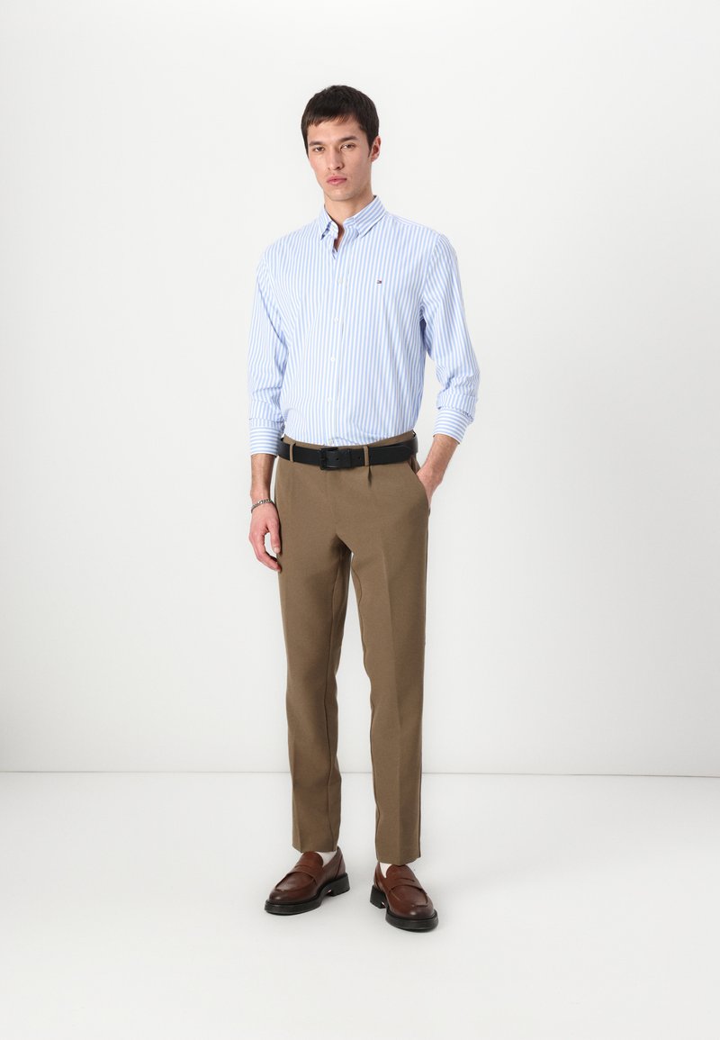Chemise à rayures bleu clair et blanche avec des boutons, pantalon beige, ceinture noire et mocassins marron. Coupe nette et ajustée, avec une texture lisse.
