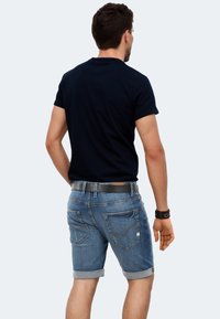 Dark navy t-shirt paired with light blue denim shorts. Shorts feature rolled cuffs, back pockets, and a leather belt with silver buckle.