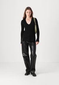 Haut en tricot noir côtelé à manches longues avec un décolleté en V, assorti à un pantalon en cuir noir brillant et un sac à main vert. Des chaussures noires plates complètent le look.
