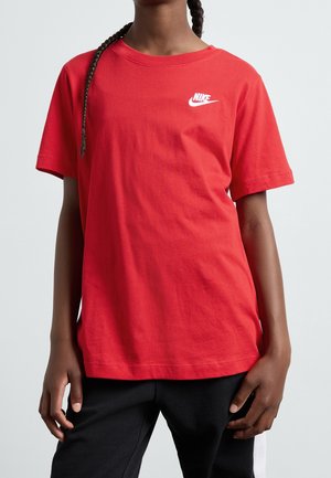 Person iført en rød Nike t-shirt og sorte bukser, med flettet hår synligt på venstre side.
