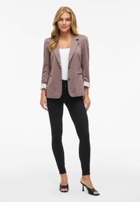 Svetle fialový blazer s přizpůsobeným střihem, s detaily na knoflících a ohrnutými rukávy, v kombinaci s černými úzkými džíny a černými botami na otevřenou špičku.