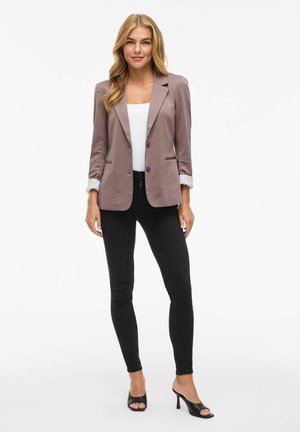 Svetle fialový blazer s přizpůsobeným střihem, s detaily na knoflících a ohrnutými rukávy, v kombinaci s černými úzkými džíny a černými botami na otevřenou špičku.