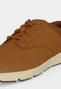Gros plan sur une chaussure à lacets en cuir marron avec des surpiqûres détaillées et une semelle en caoutchouc beige clair.