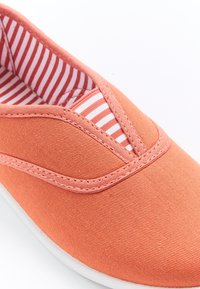 Zapato tipo slip-on de lona coral con detalles elásticos blancos, con forro a rayas rojas y blancas y una superficie texturizada.
