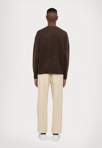 Brown knitted sweater with a relaxed fit, ribbed hem, and back seam detail, paired with cream-colored wide-leg trousers and white sneakers.