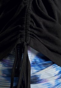Gros plan d'un tissu noir froncé avec cordons sur un matériau texturé à motifs bleu, blanc et violet.