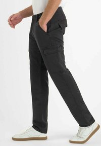 Zwarte cargobroek met zijzakken, tapered fit en dubbel gestikte naden, gecombineerd met witte sneakers met een gumrubberen zool.