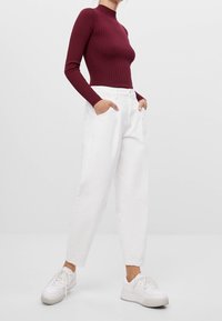 Haut bordeaux à manches longues côtelé associé à un jean blanc ample et des baskets blanches. La tenue présente une silhouette ajustée et un design décontracté.