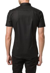 Camisa negra de mangas cortas con cuello puntiagudo, textura suave, corte entallado y dobladillo curvado, exhibida desde la parte posterior.