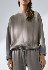 Grijze sweatshirt met een losse pasvorm, voorzien van een ronde hals, trekkoord in de zoom en een zachte textuur, gecombineerd met bijpassende broek.