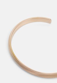 Metal cuff bracelet in rose gold with a smooth surface and subtle textured diagonal grooves along one edge. Minimalist design, open-ended.