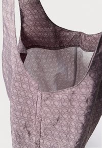 Večkratno uporabna torba v svetlo vijolični barvi z teksturiranim vzorcem prepletajočih se oblik. Notranjost je obložena z gladkim materialom, ki povečuje vzdržljivost.