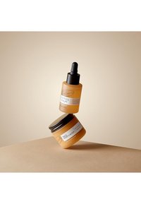 Two skincare products: a droplet bottle of orange serum with a black dropper, and a jar of orange face moisturizer with a black lid.