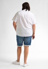 Witte short-sleeve shirt met een achterste schouderdeel, gecombineerd met blauwe denim shorts die aan de zoom zijn opgerold, en witte sneakers met rode accenten.