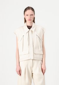 Gilet senza maniche beige chiaro con colletto alto, chiusura frontale con zip e due tasche anteriori dotate di cerniere diagonali. Tessuto liscio e strutturato.