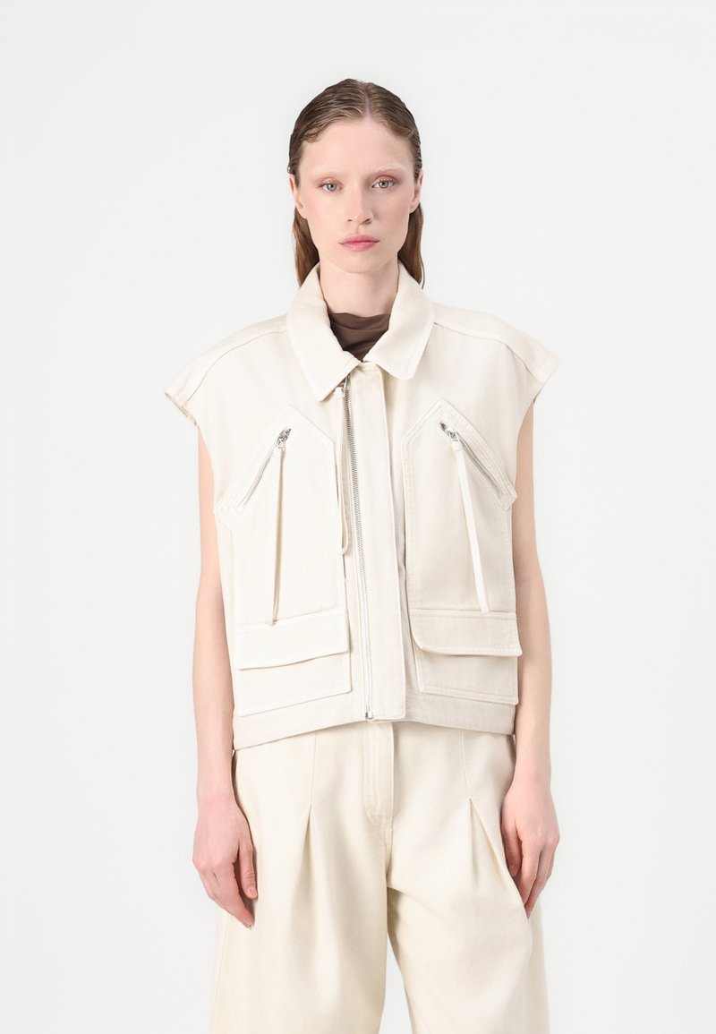 Gilet senza maniche beige chiaro con colletto alto, chiusura frontale con zip e due tasche anteriori dotate di cerniere diagonali. Tessuto liscio e strutturato.