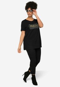 Černé bavlněné tričko s designem "MAGIC" ve zlatém provedení, v kombinaci s černými legínami se šněrovacími detaily a černými polokozačkami na podpatku.