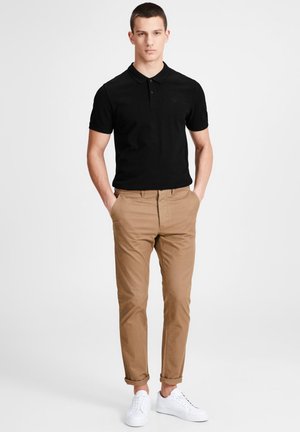 Polo noir avec un col, associé à un pantalon chino beige et des baskets blanches. Design simple et palette de couleurs neutres.
