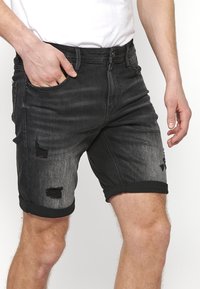 Crne traper kratke hlače s ispucalim i rastrganim rubovima, s preklopljenim rubom, pet džepova i slim fit dizajnom.