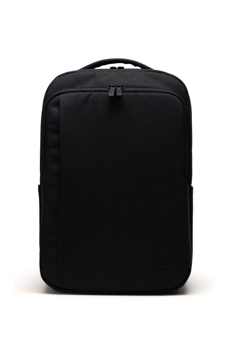 Mochila negra con una textura de tela suave, forma rectangular, doble cremallera y un discreto parche de la marca en la parte frontal.