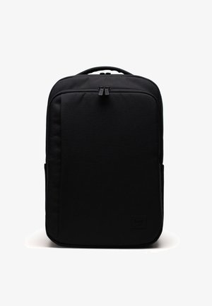Mochila negra con una textura de tela suave, forma rectangular, doble cremallera y un discreto parche de la marca en la parte frontal.