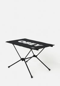 Zwarte draagbare kampeertafel met een vlakke oppervlakte waarop het woord "OBEY" in vetgedrukte witte letters staat, ondersteund door een opvouwbaar metalen frame.
