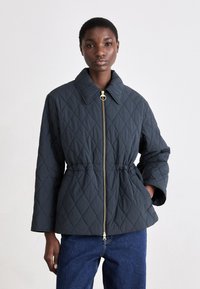 Κοντό γκρι μπουφάν με ανάγλυφο σχέδιο και χρυσό φερμουάρ, γιακά σε σχήμα πόνυ και ελαστική μέση. Διαθέτει φαρδιές μανσέτες και διακοσμητικό σχέδιο διαμαντιών.