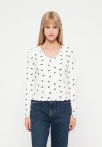 Λευκή μπλούζα με μακριά μανίκια και ριπ ύφανση, διαθέτει σκαλπμένο στρίφωμα, V-λαιμόκοψη και μικρά σκούρα μπλε λουλούδια σε όλη την επιφάνεια.