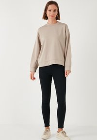 Felpa beige con vestibilità morbida, colletto rotondo e polsini a coste, abbinata a jeans skinny neri e sneakers beige. Design semplice.